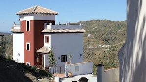 A two-story building with a red and white facade, a tiled roof, and a view of a hilly landscape in the background. - Villa La Posada, Canillas de Albaida (Canillas de Albaida)