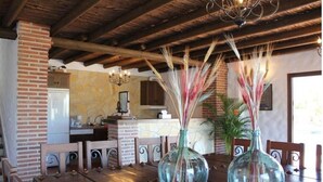 A dining area with a wooden table, two glass vases with dried plants, a brick wall, and a kitchen in the background. - Villa La Posada, Canillas de Albaida (Canillas de Albaida)