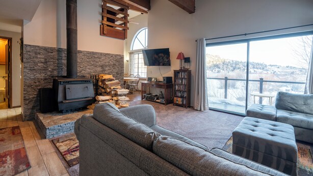 Un salón con chimenea, un sofá, un televisor y un ventanal con vistas.