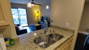 A kitchen with granite countertops, stainless steel sinks, and a dishwasher. There is a window with a view of parked cars outside. - PRIVATE CONDO IN BEAUTIFUL GATED COMMUNITY IN SEVEN HILLS (Henderson)
