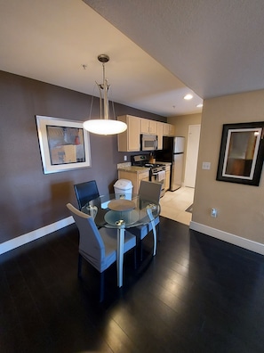 A modern kitchen with dark wood flooring, a dining area with a glass table and chairs, and a kitchen island.