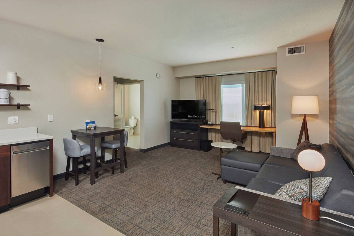 A hotel room with a kitchenette, a dining area, a living room with a sofa and TV, and a bathroom.