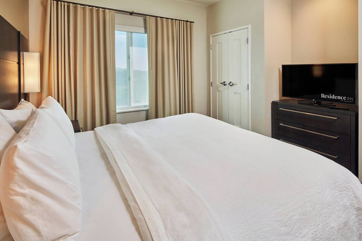 A hotel room with a large bed, a television, a wardrobe, and a window with curtains.