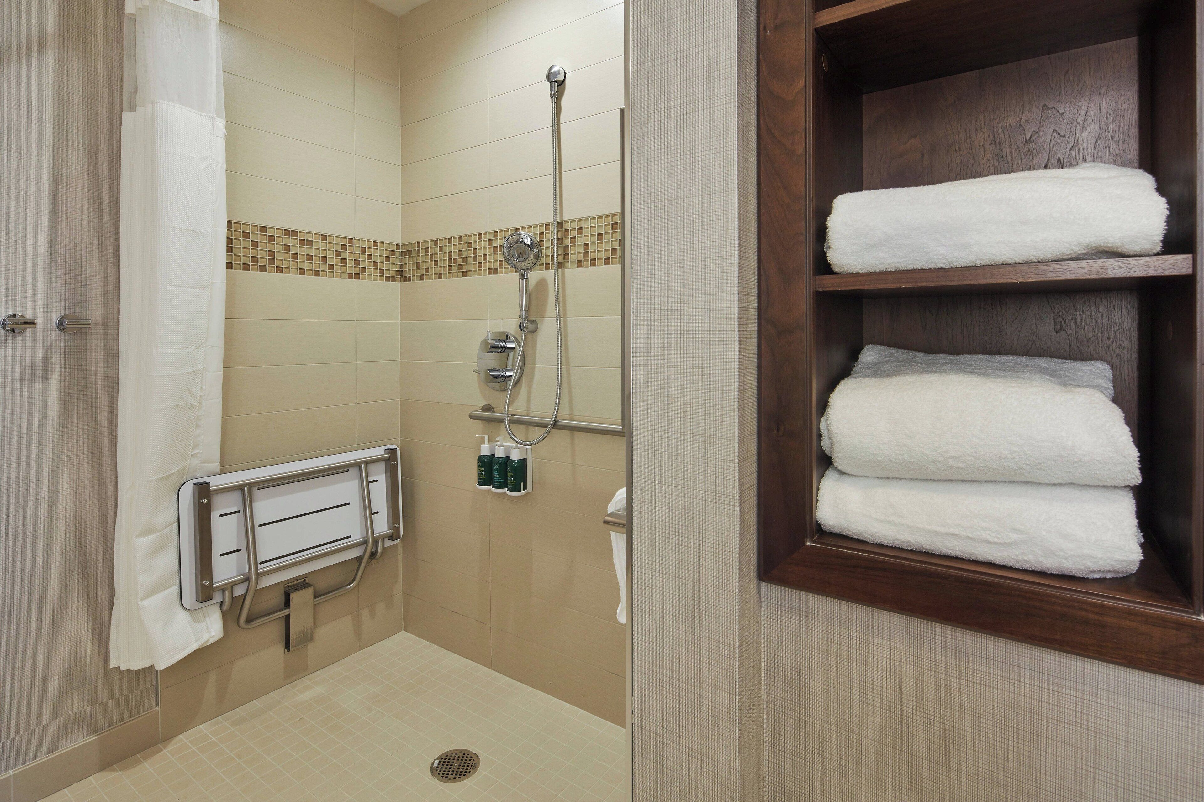 A bathroom with a shower, a towel rack, and a shelf with folded towels.