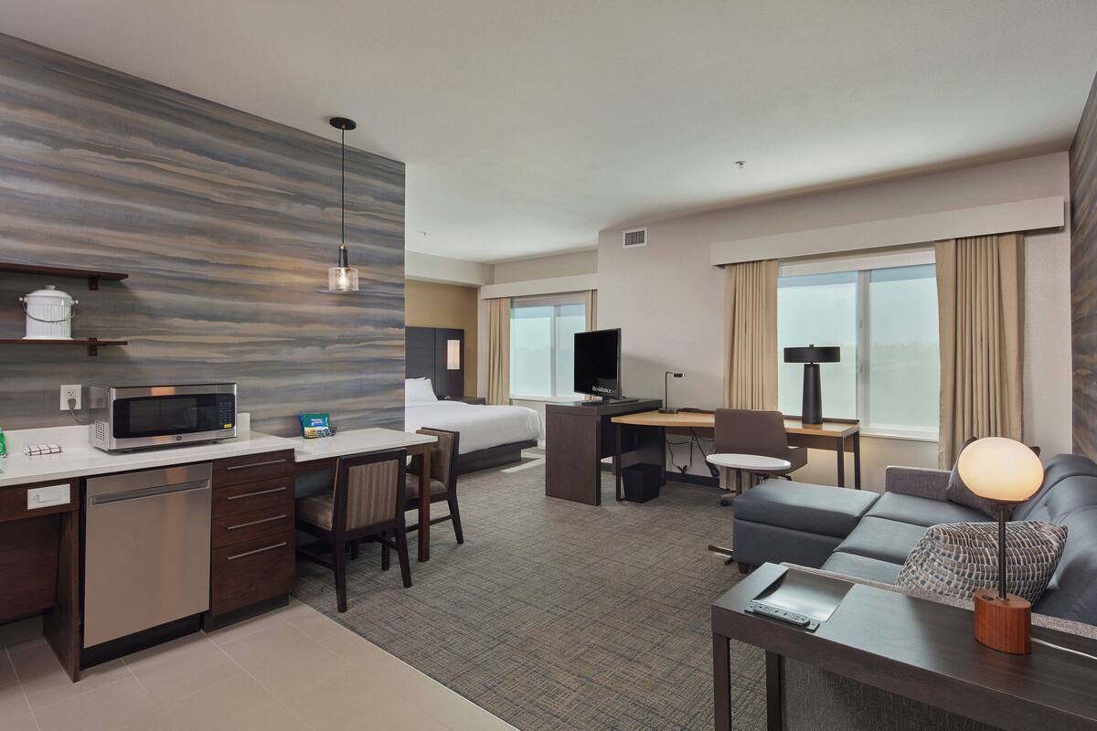 A hotel room with a kitchenette, a bed, a desk, a sofa, and a TV.