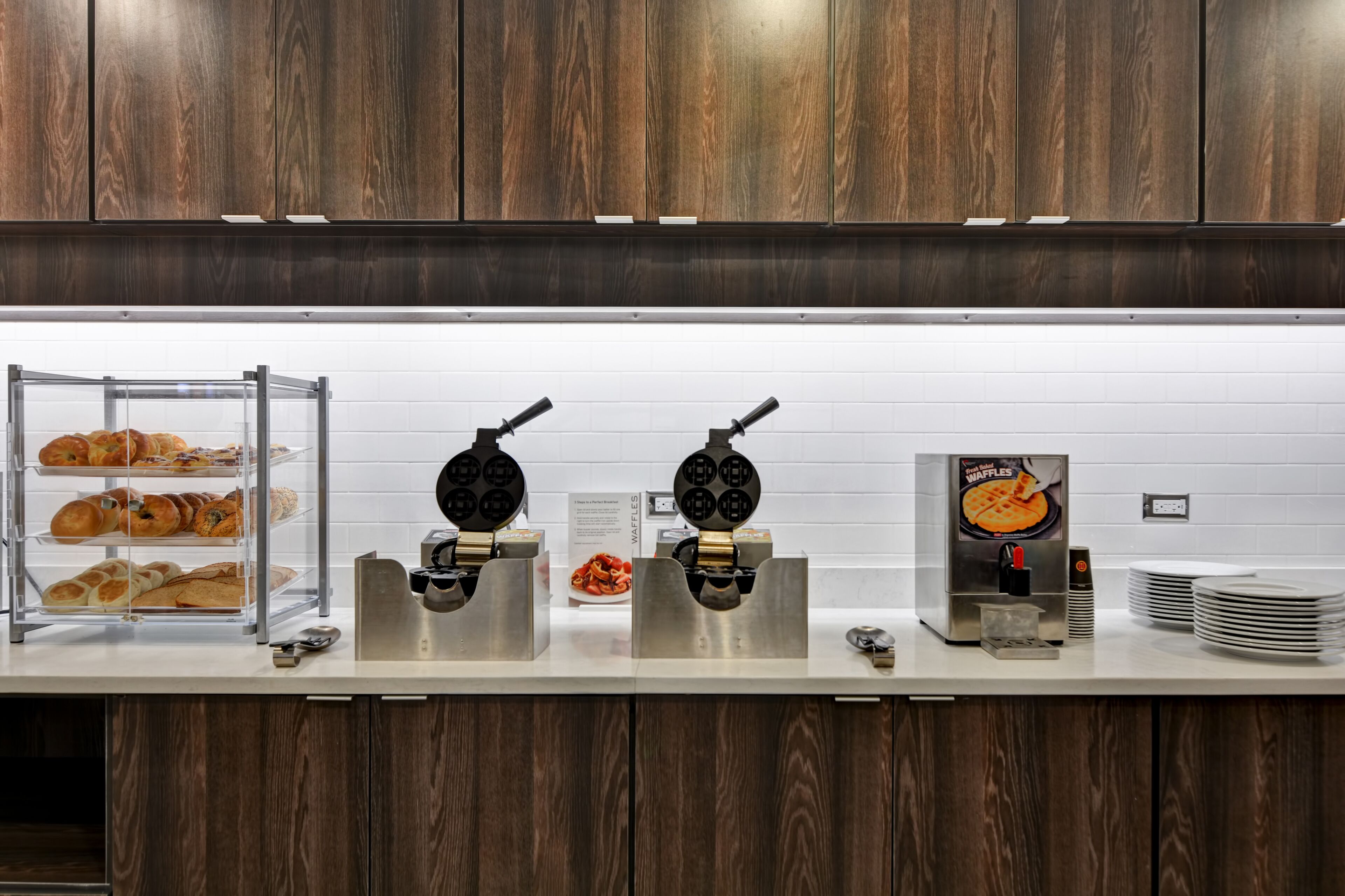 Un buffet pour le petit-déjeuner avec des gaufriers, un espace dédié aux gaufres et un présentoir à pains.