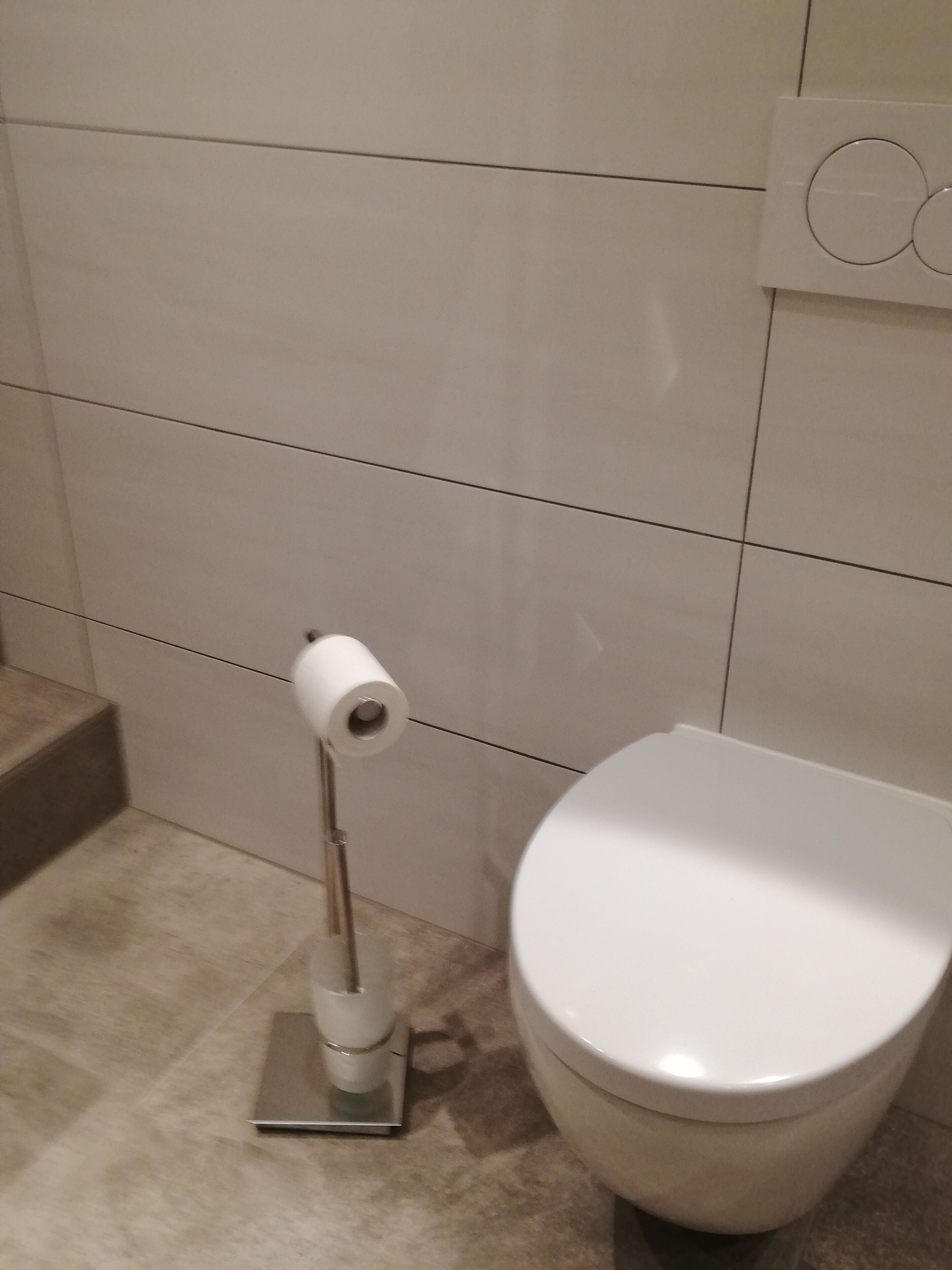 Des toilettes avec un abattant blanc et un porte-rouleau de papier toilette.