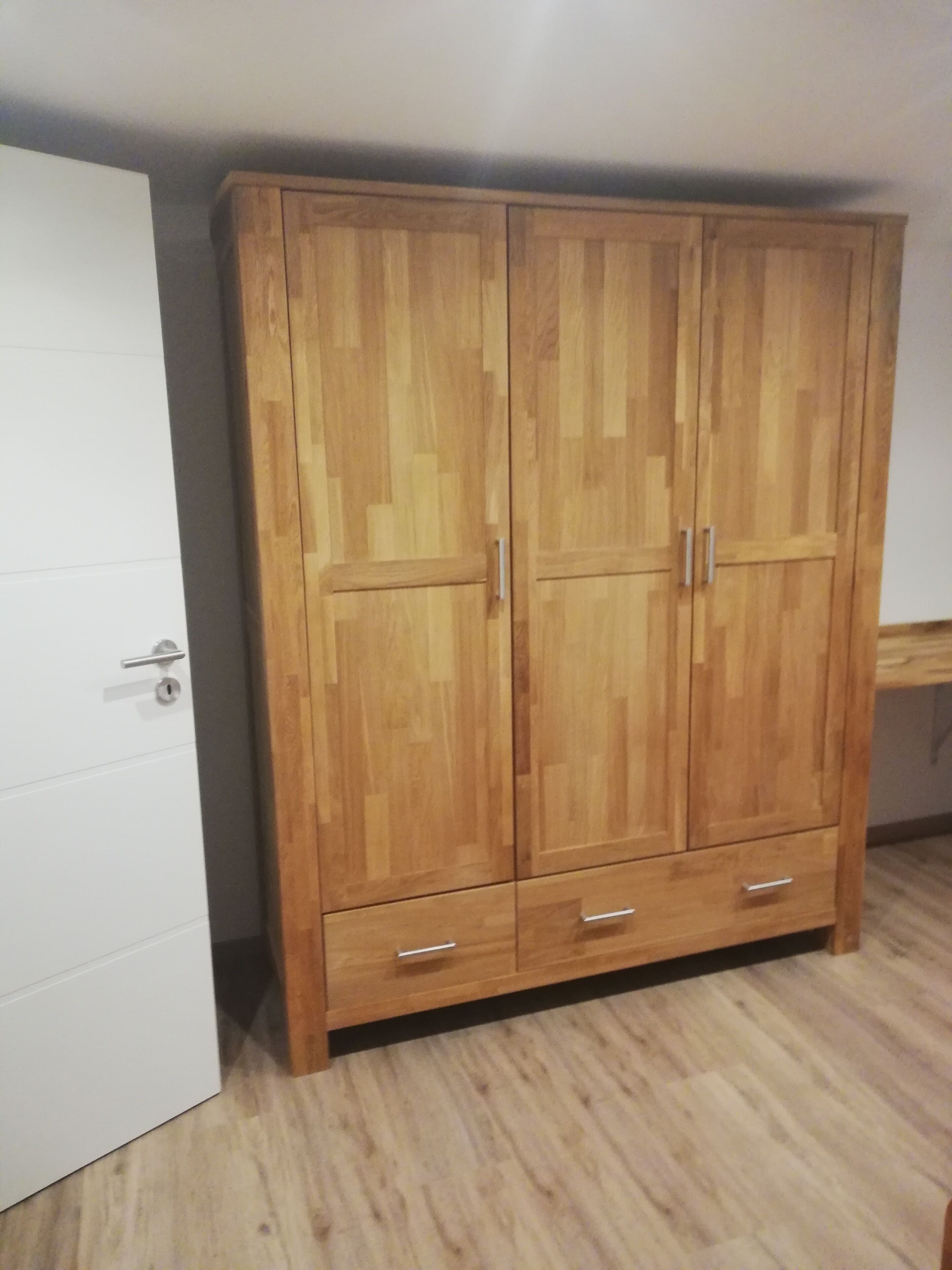 Un armario de madera con dos puertas y dos cajones, ubicado junto a una puerta blanca.