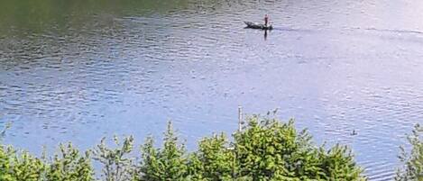 Un lac avec un bateau et une personne dans l’eau. On aperçoit des arbres et une colline en arrière-plan.