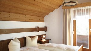 Un lit double avec une tête de lit en bois, deux tables de chevet avec des lampes, un plafond en bois et une fenêtre avec des rideaux.