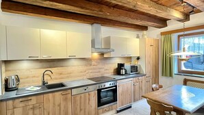 Une cuisine moderne avec des meubles en bois, un évier en acier inoxydable, un four encastré et un coin repas comprenant une table et des chaises.