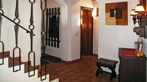 Un escalier avec des rampes en métal, un plafond en bois, un couloir avec une porte et une lampe fixée au mur.