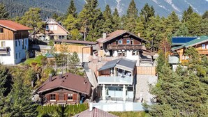 Un village de montagne avec des maisons traditionnelles en bois, un bâtiment moderne et une vue sur des montagnes enneigées.