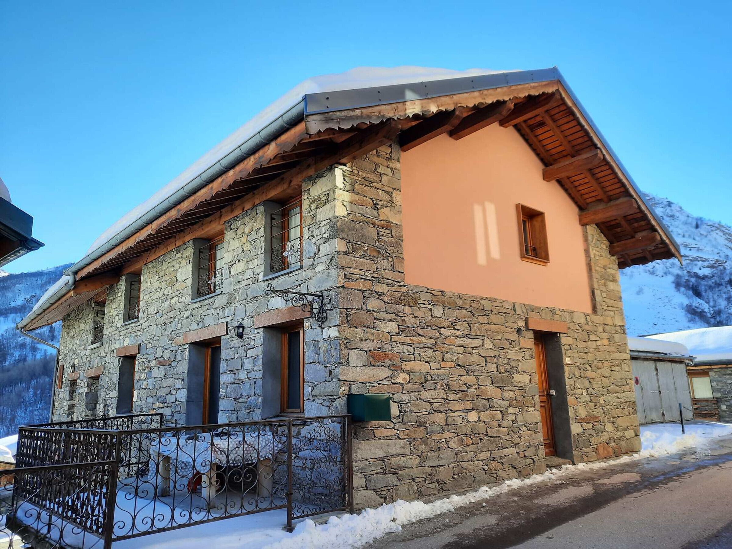 A stone building with a wooden roof and a small balcony, surrounded by snow and mountains.