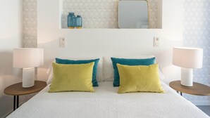 Een verzorgde hotelkamer met een bed, twee nachtkastjes, een spiegel en twee wandlampen.