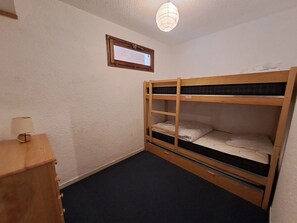 A small, single-bunk room with a wooden bunk bed, a small desk with a lamp, and a framed certificate on the wall.
