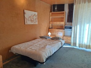 A bedroom with a bed, a painting, a television, and a microwave.