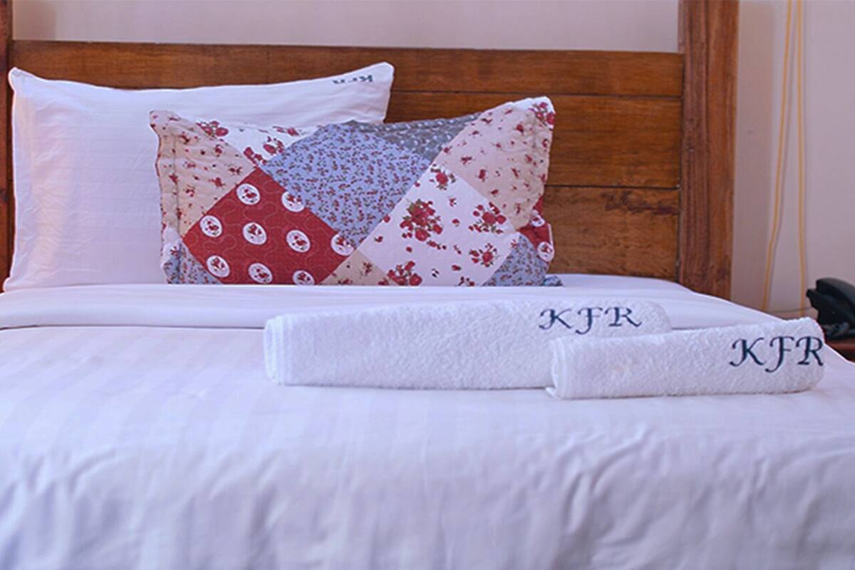 Un lit bien fait, avec des draps blancs, une tête de lit en bois et deux serviettes ornées de monogrammes brodés.