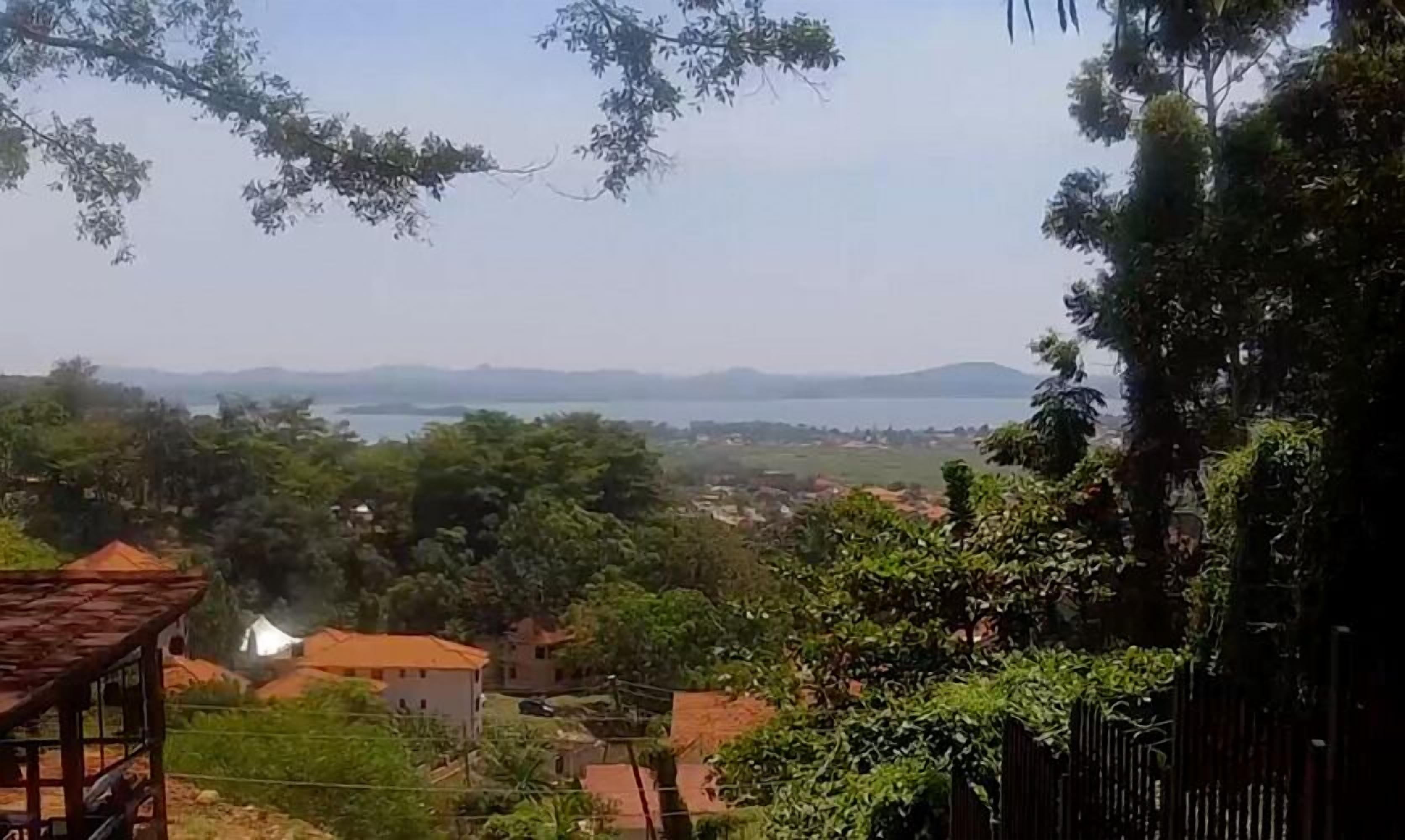 A rural landscape with a view of a lake and distant mountains. There are houses and trees in the foreground.