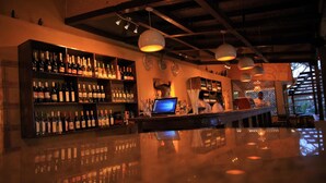 Una zona de bar con estantes llenos de botellas, un ordenador portátil sobre la barra y un techo rústico.