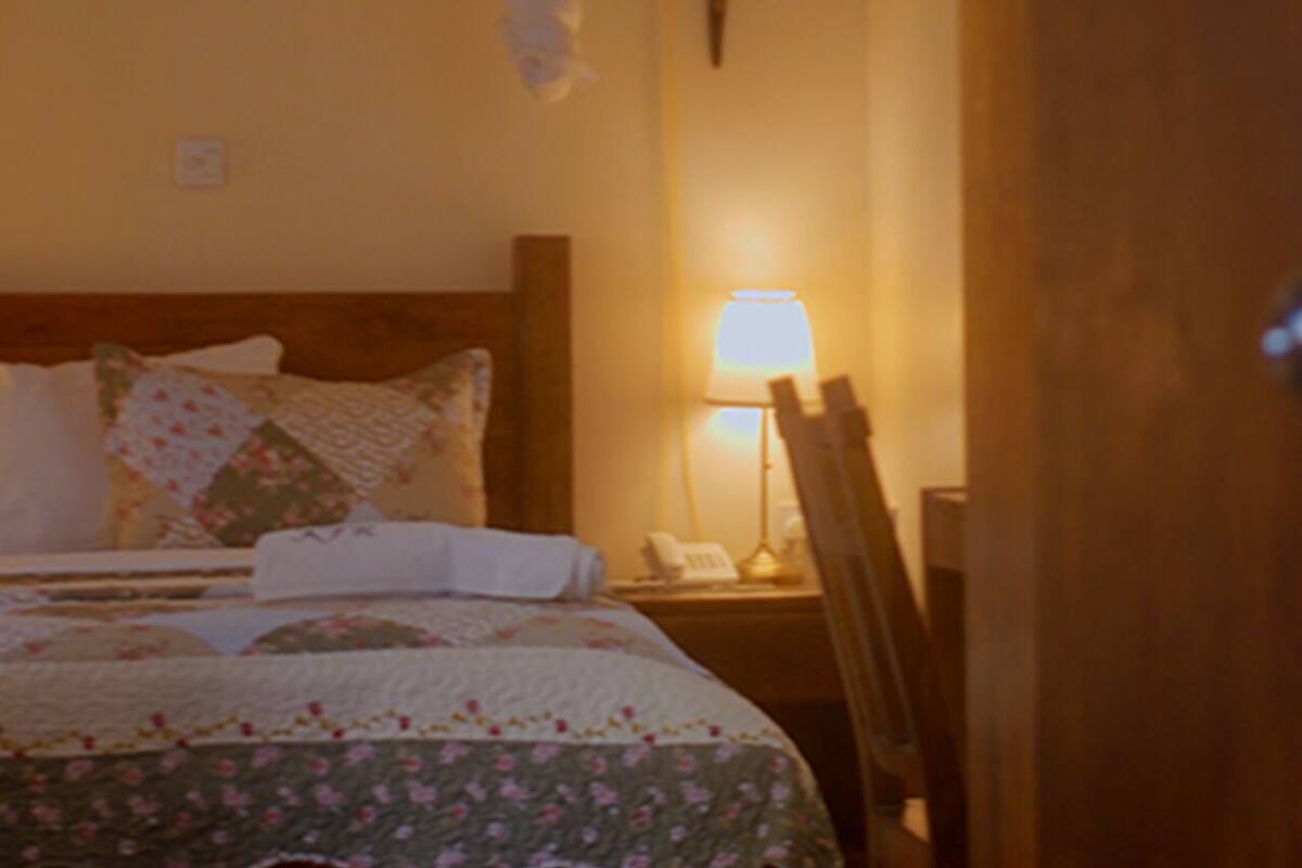 Un lit bien fait, recouvert d’une couvre-lit à motifs floraux, une lampe de chevet et un téléphone sur la table de nuit.