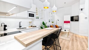 Una cocina moderna con armarios blancos, encimera de madera, taburetes negros y lámparas colgantes.