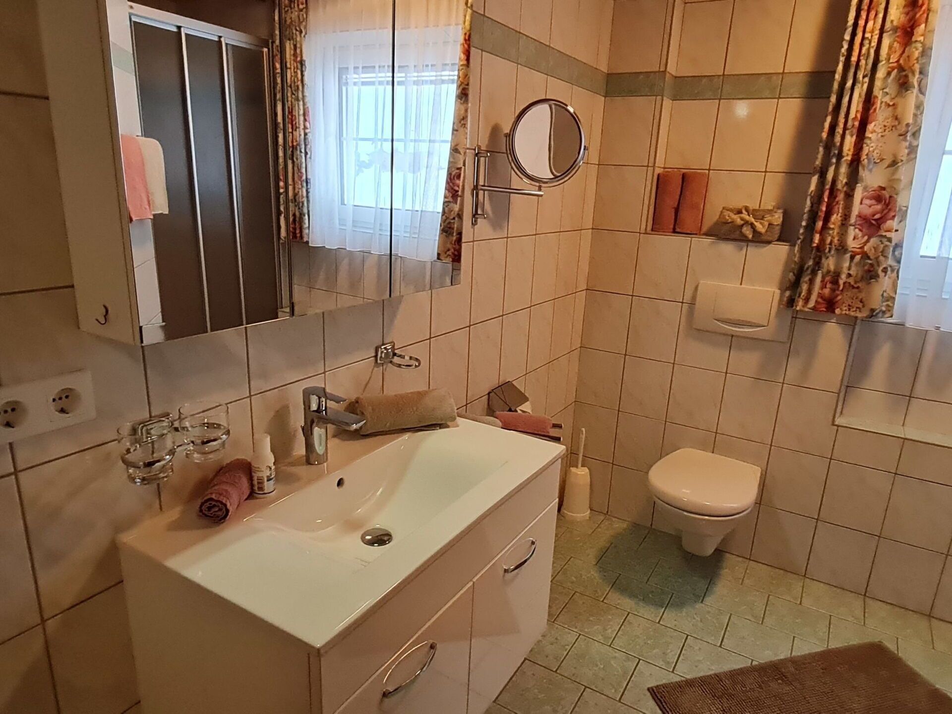 Et badeværelse med vask, spejl, toilet og håndklædestang.