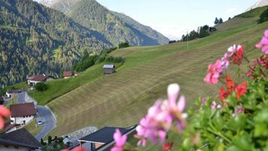 Ländliche Landschaft mit einem Haus an einem Hügel, umgeben von Bergen und Grün.