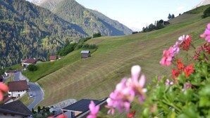 A rural village with houses on a hillside, surrounded by mountains and greenery.