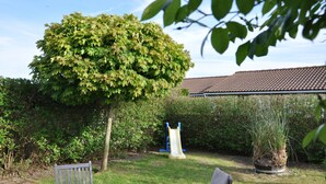 A garden with a tree, a slide, and a table. - The Happy House (De Haan)