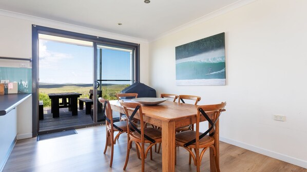 A dining area with a table and chairs, a view through a glass door, and a painting on the wall.