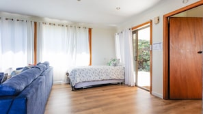 A bedroom with a bed, a blue sofa, wooden flooring, and a wooden door.