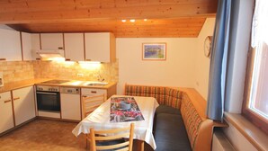 A compact kitchen with wooden cabinets, a stove, and a sink. There is a dining table with chairs and a bench with a cushion. A framed picture hangs on the wall. - Nice apartment for 5 guests with WIFI, TV, patio and pets allowed (Gaschurn)