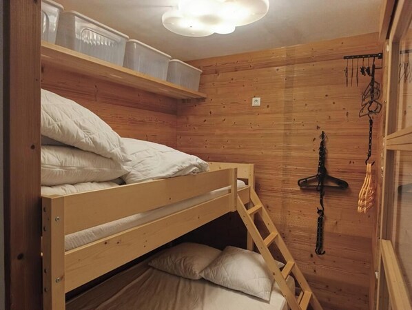 Et soveværelse med køjesenge, træpaneler, loftslampe og opbevaringskasser.