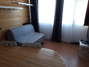 A room with a wooden wall, a grey sofa, a dining table, and a TV on a stand. - Studio renovated (Orcières Merlette)