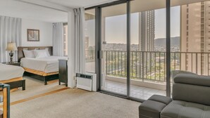 A hotel room with a bed, bedside table, lamp, air conditioning unit, and a view of the city through large windows. - Excellent Diamond Head View Condo - Remodeled, Free Parking! (Honolulu)