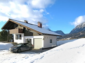A two-story house with a sloped roof, a car parked in front, and snow-covered ground.