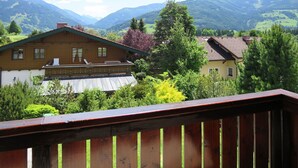 Una casa de fusta amb un balcó, envoltada de vegetació exuberant i muntanyes al fons.