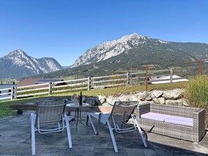 Ein Sitzbereich im Freien mit Stühlen und einem Tisch, mit Blick auf eine gebirgige Landschaft.