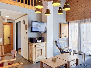 A modern living room with a flat-screen TV, wooden furniture, and pendant lighting.
