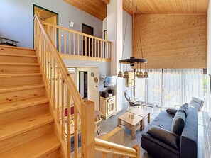 A wooden staircase leading to a loft bedroom with a television and a dining area with a table and chairs.