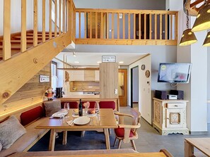 A wooden staircase leading to an upper level, a dining area with a table set for two, and a television on a cabinet.