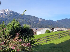 Ländliche Landschaft mit Holzzaun, einem kleinen Gebäude und einem Gebirge im Hintergrund.