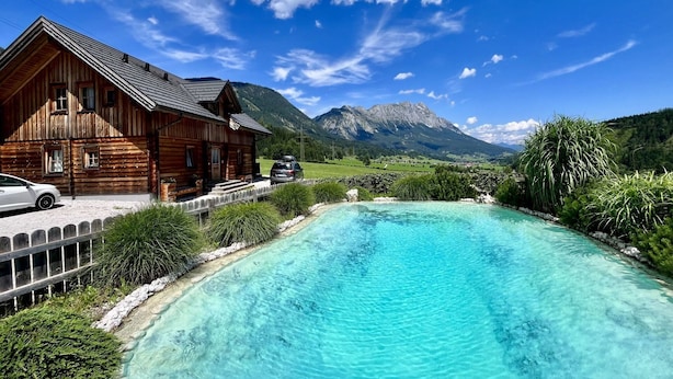 A wooden cabin with a swimming pool surrounded by lush greenery and mountains in the background. - Cosy apartment in villa for 18 guests with WIFI, pool, TV, terrace and pets allowed (Klazenberg)