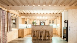 A modern kitchen with wooden cabinetry, a central island with stools, and a built-in stove. - Cosy apartment in villa for 18 guests with WIFI, pool, TV, terrace and pets allowed (Klazenberg)