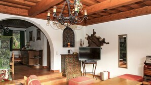 Un soggiorno tradizionale con un tavolo in legno, poltrone rosse imbottite, un televisore su un mobile e un lampadario.