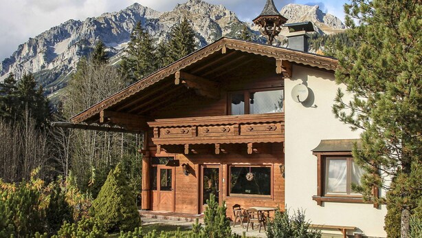 Un chalet in legno con balcone, ampie finestre e lo sfondo di una montagna.