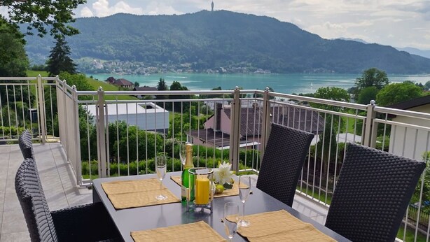 Un balcon avec une table dressée pour deux personnes, offrant une vue imprenable sur un lac pittoresque et les montagnes.
