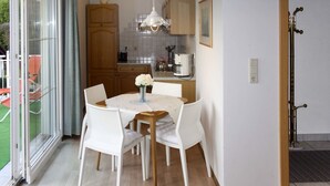 Un coin repas avec une table dressée pour quatre personnes, entourée de chaises blanches, d’un luminaire suspendu et offrant une vue sur un jardin à travers des portes vitrées.