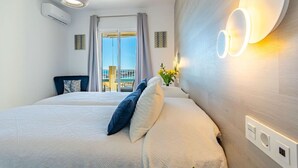 A hotel room with a large bed, a ceiling light, a wall-mounted air conditioning unit, and a view of the outdoors.